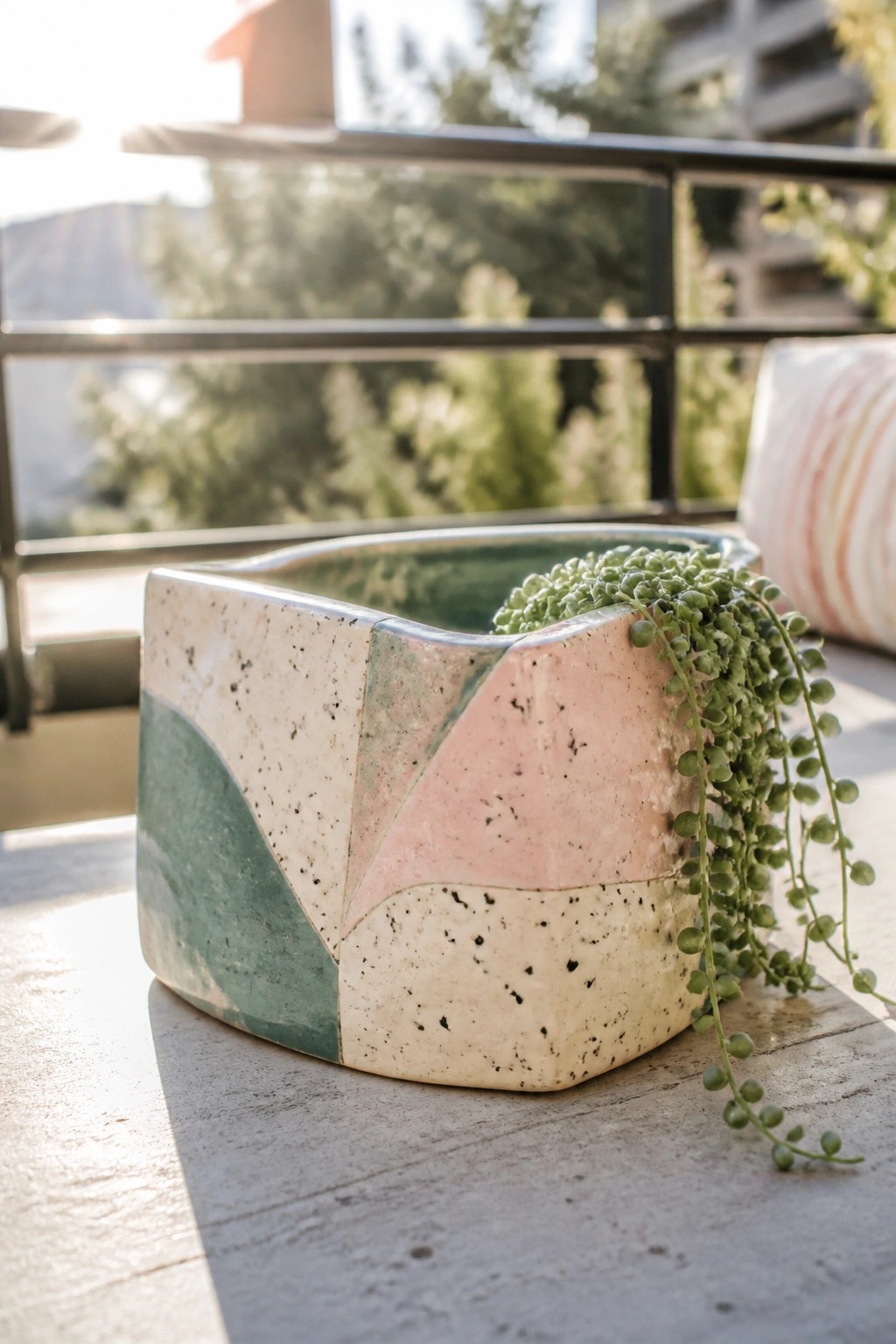 Geometric pink and green ceramic planter with trailing succulent on wooden balcony table