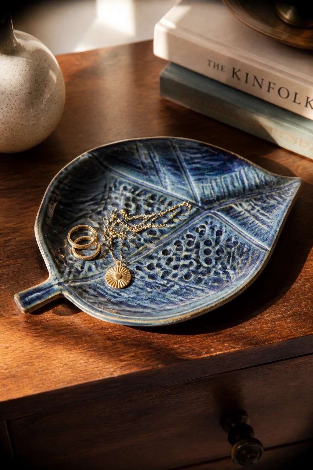 Blue ceramic leaf tray holding gold rings and sunburst necklace on wood table