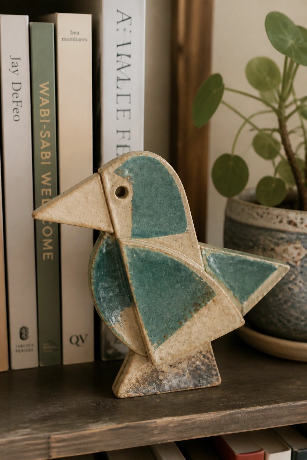 Abstract teal ceramic bird sculpture on wooden shelf with books and plant
