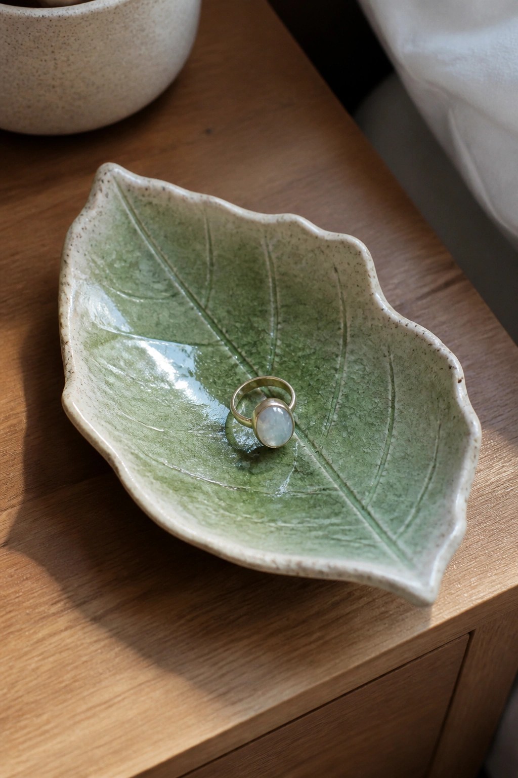 Gold ring with pale stone in green leaf-shaped ceramic bowl on wood
