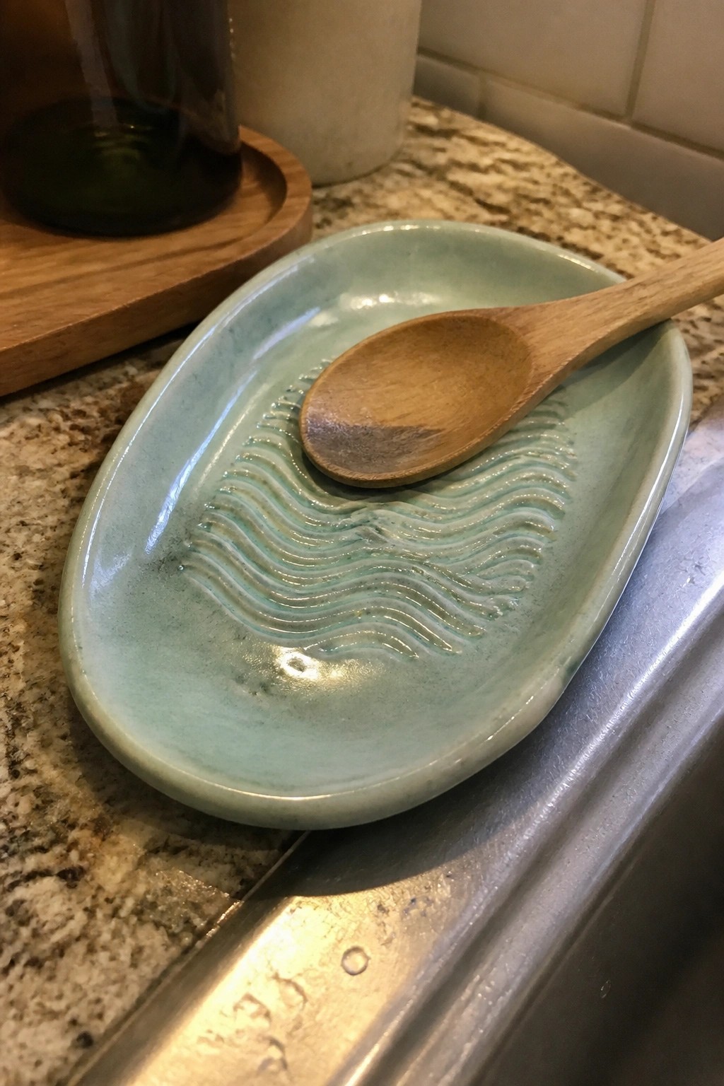 Light blue-green ceramic oval dish with wave ridges holding wooden spoon on counter