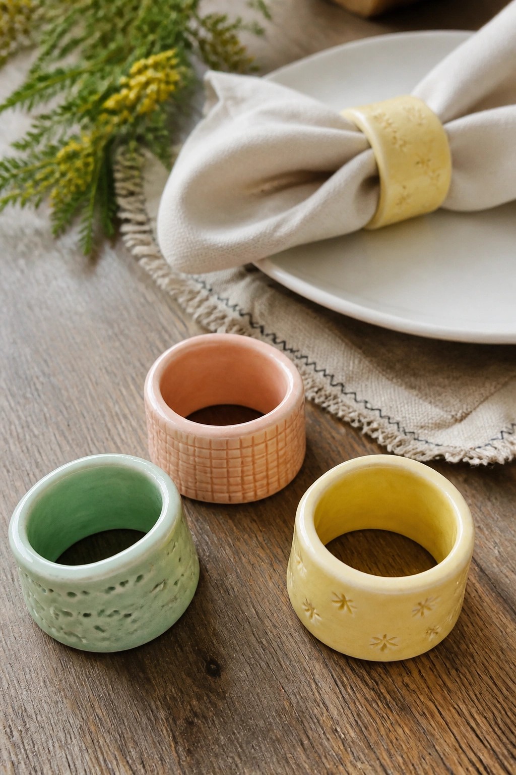 Three colorful ceramic napkin rings with embossed patterns on a wooden table setting