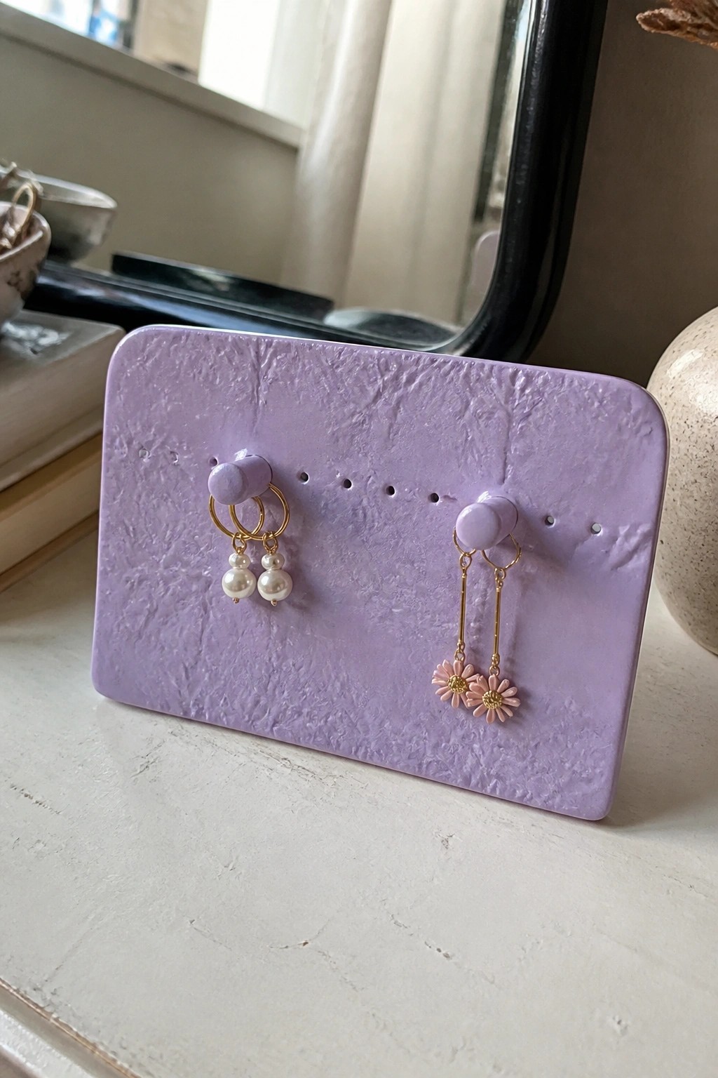 Purple display holding pearl hoop earrings and pink daisy dangles.