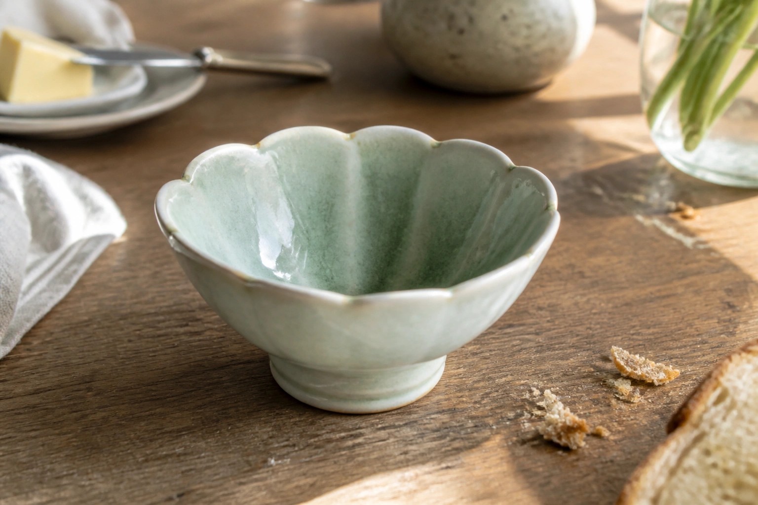 Pale green scalloped ceramic bowl on wooden table with mug nearby