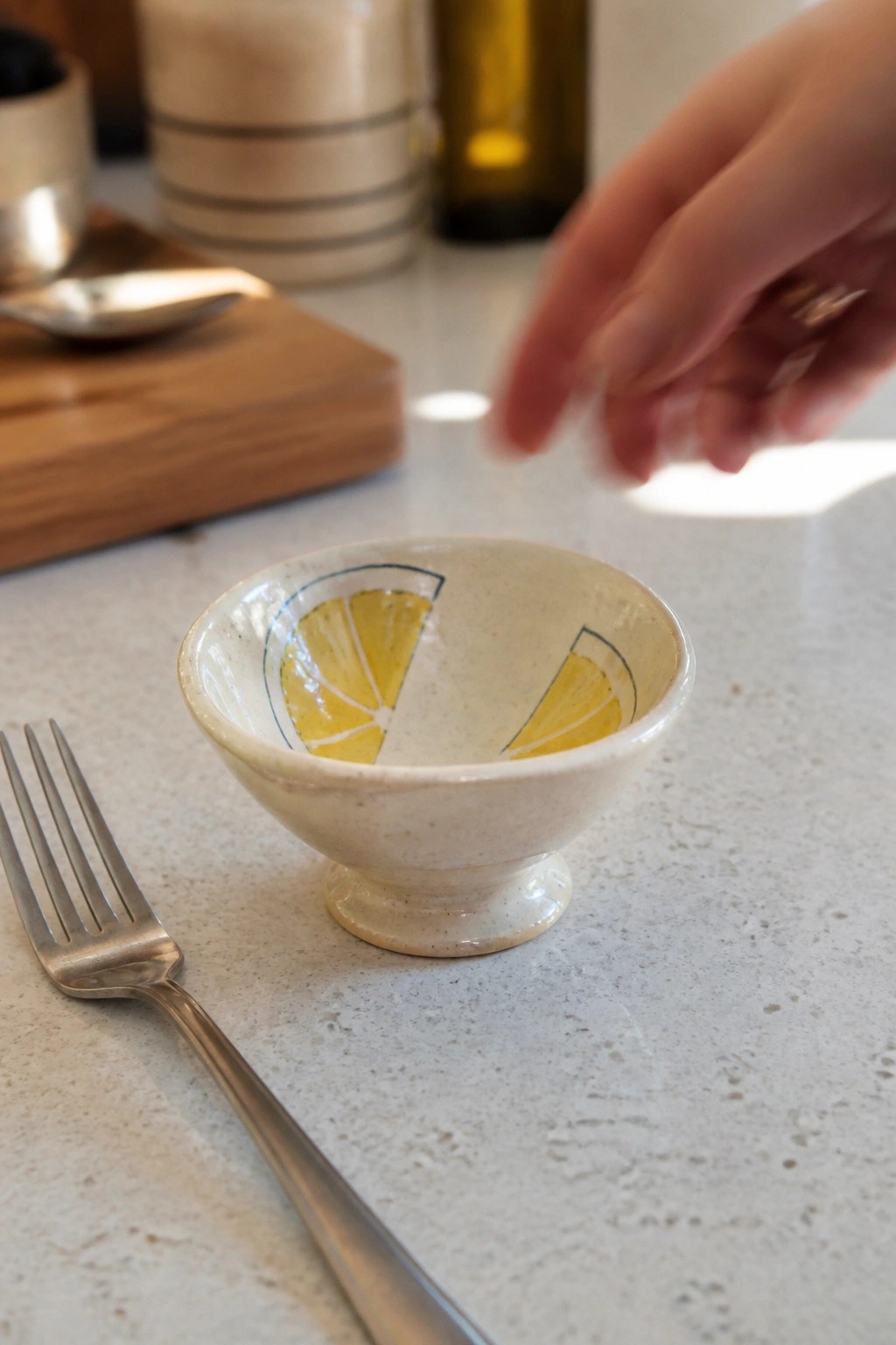 Hand reaching toward lemon-decorated bowl next to fork on white countertop