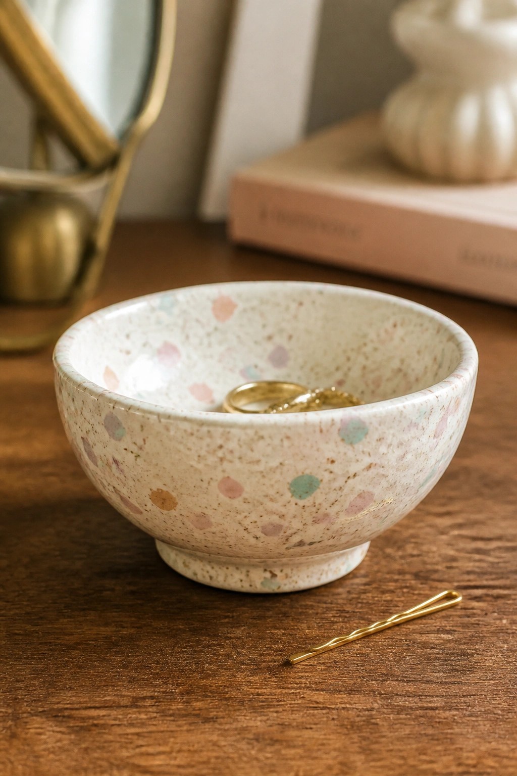 Speckled pastel bowl with gold rings beside a bobby pin on wood.