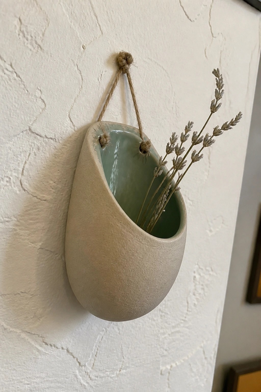 Teardrop beige ceramic vase with green interior, hung by twine holding dried lavender.