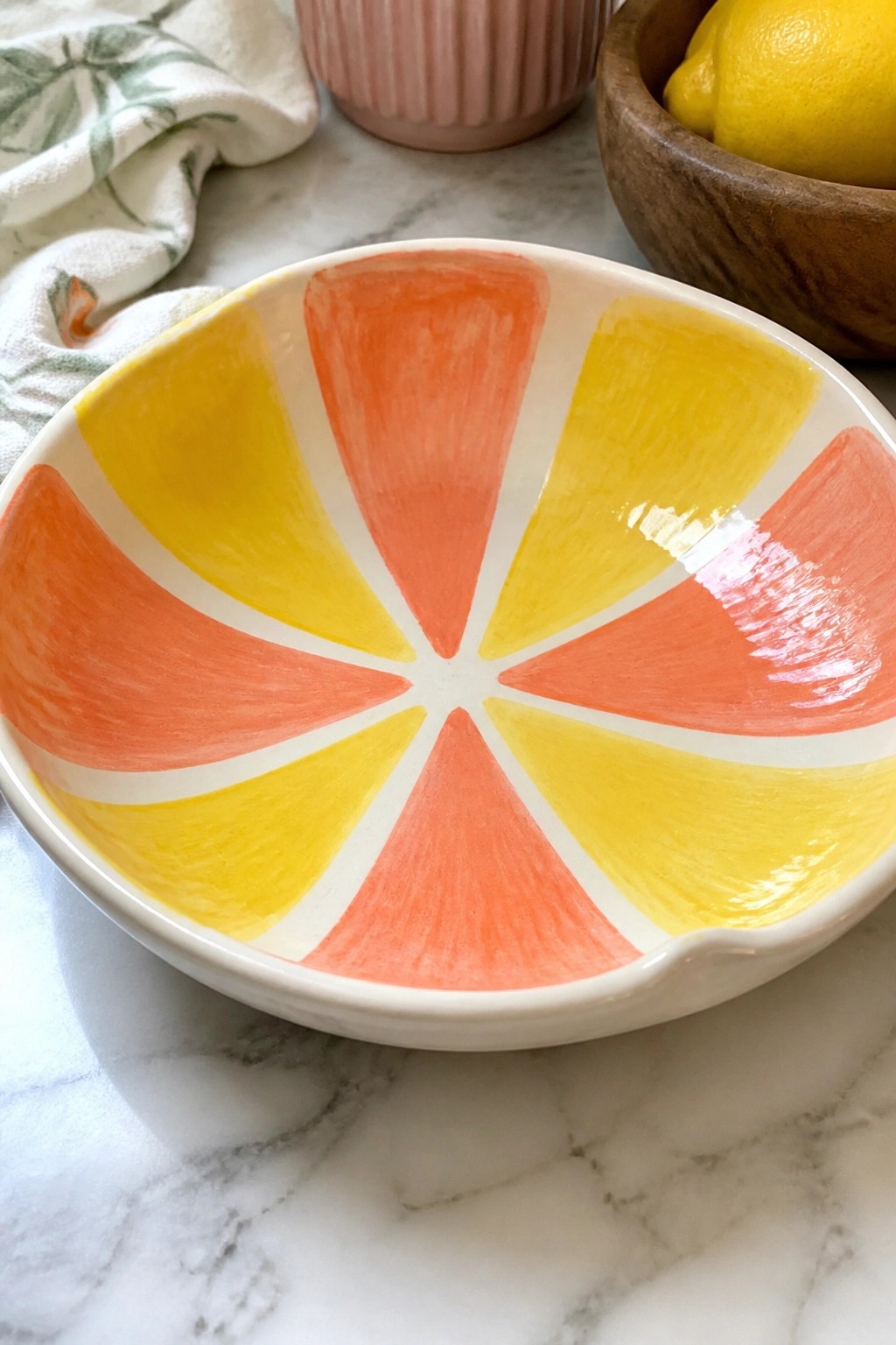 Vibrant orange and yellow citrus bowl on marble with wooden lemon bowl nearby