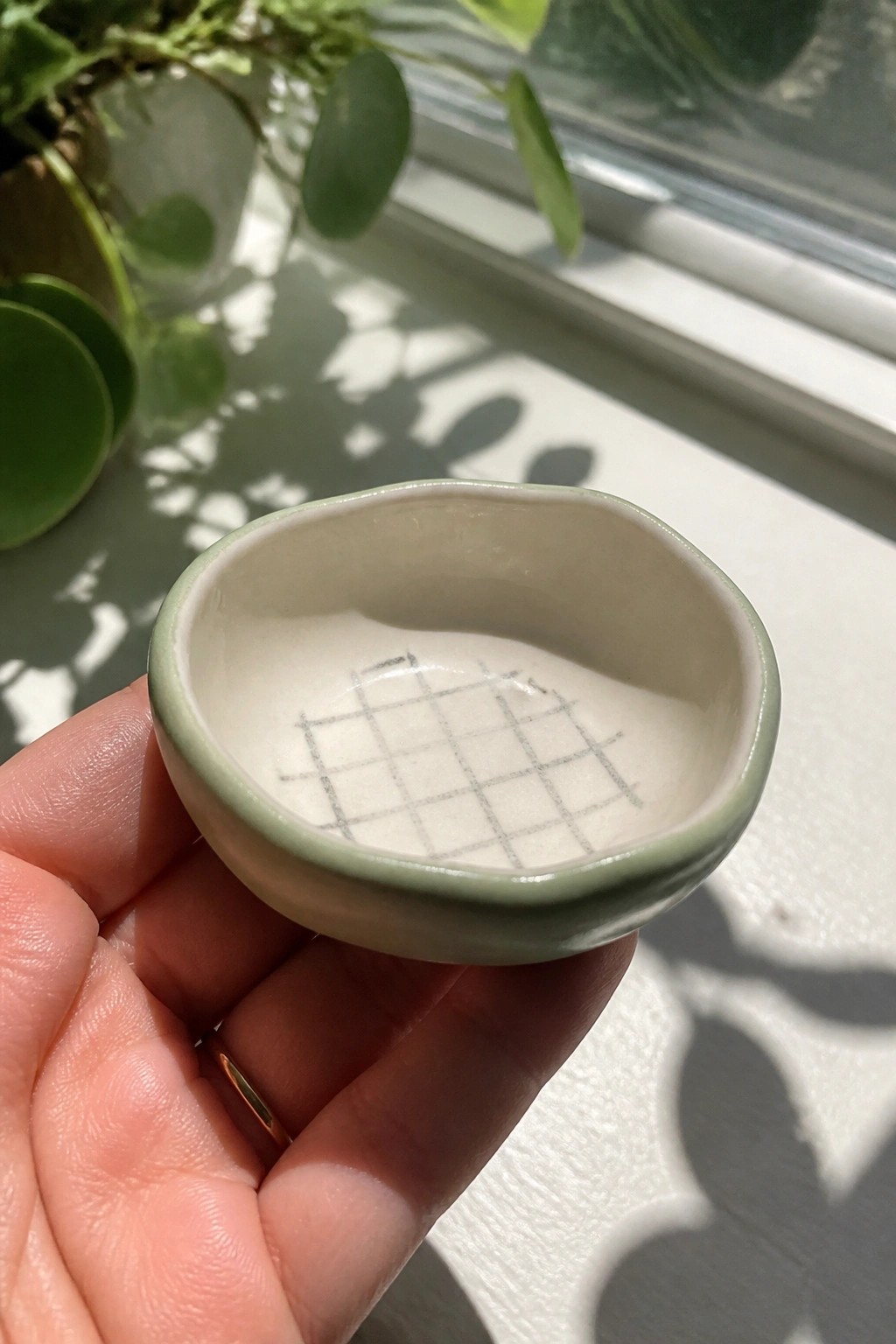 Hand with gold ring holds small green bowl with black grid inside.