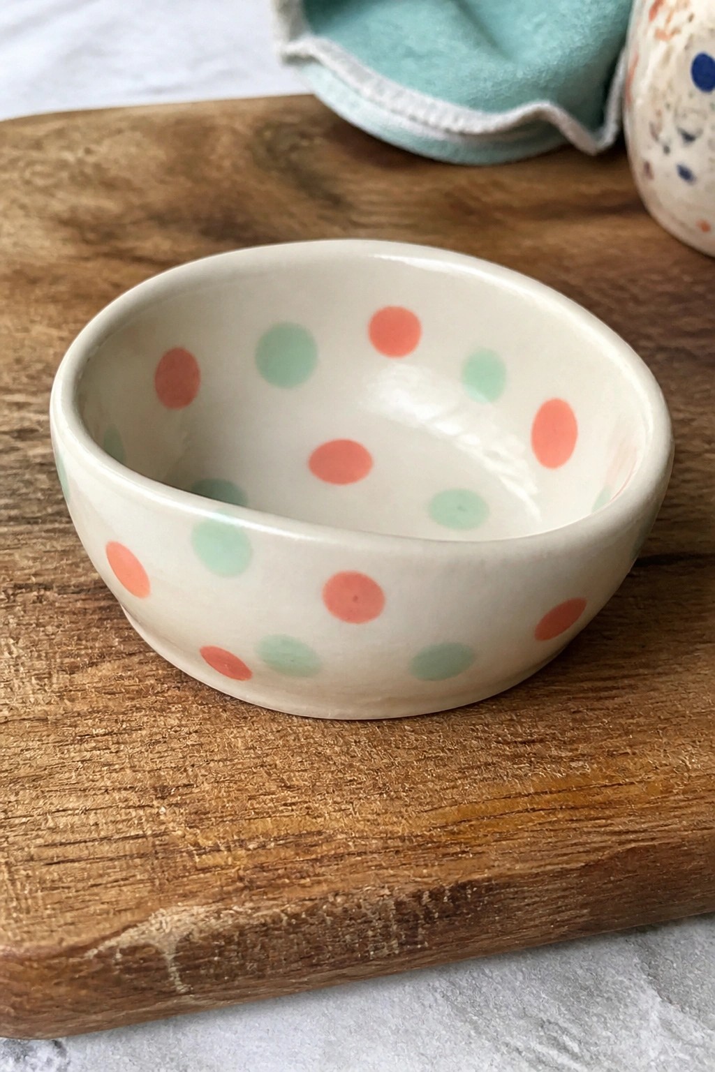 Small white bowl with coral and mint green polka dots on wood