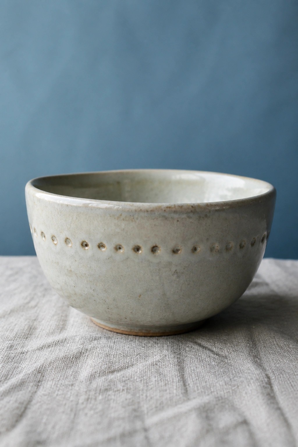 Light gray ceramic bowl with dotted rim on gray fabric against blue wall