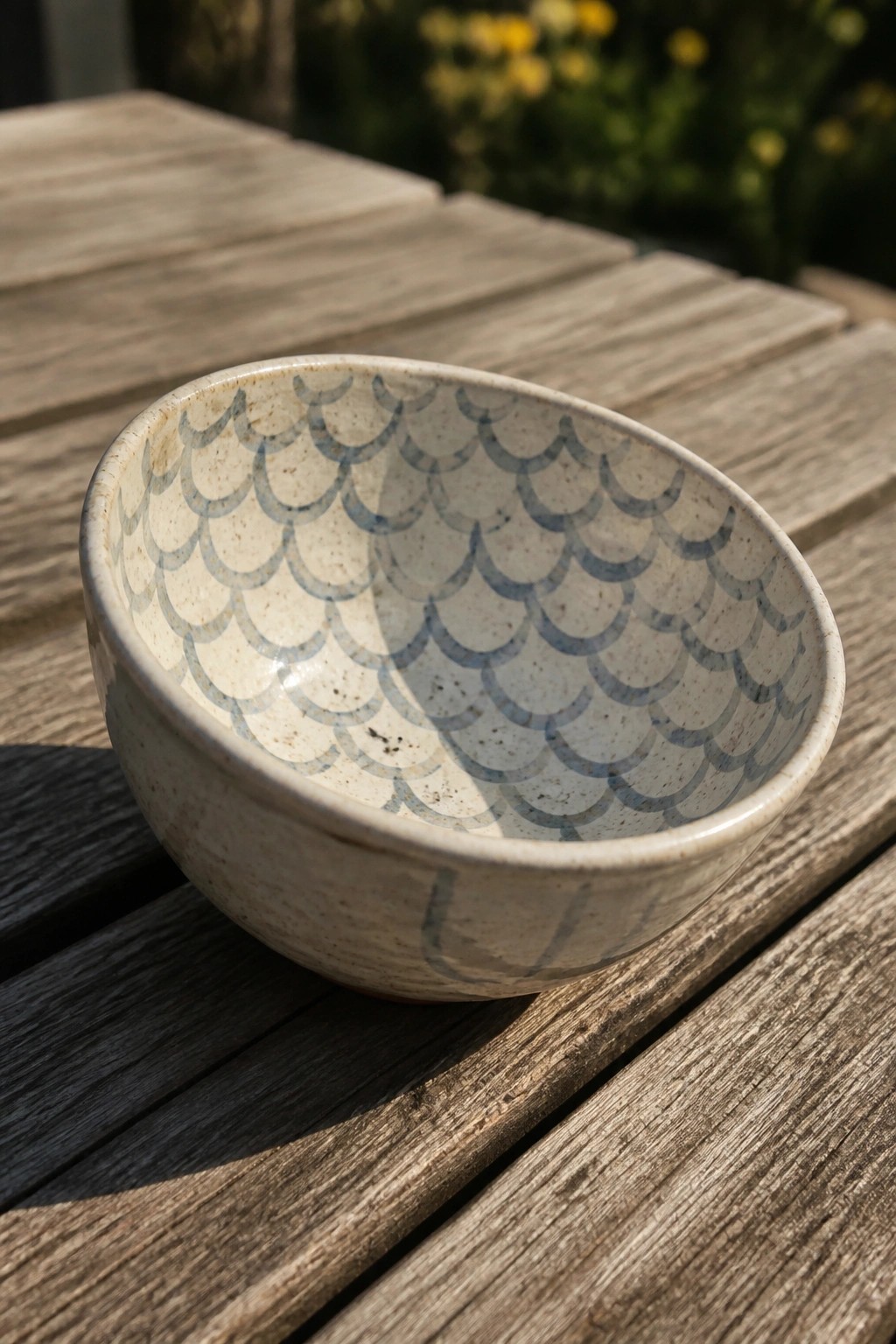 Speckled ceramic bowl with blue scallop pattern on sunlit wooden table.