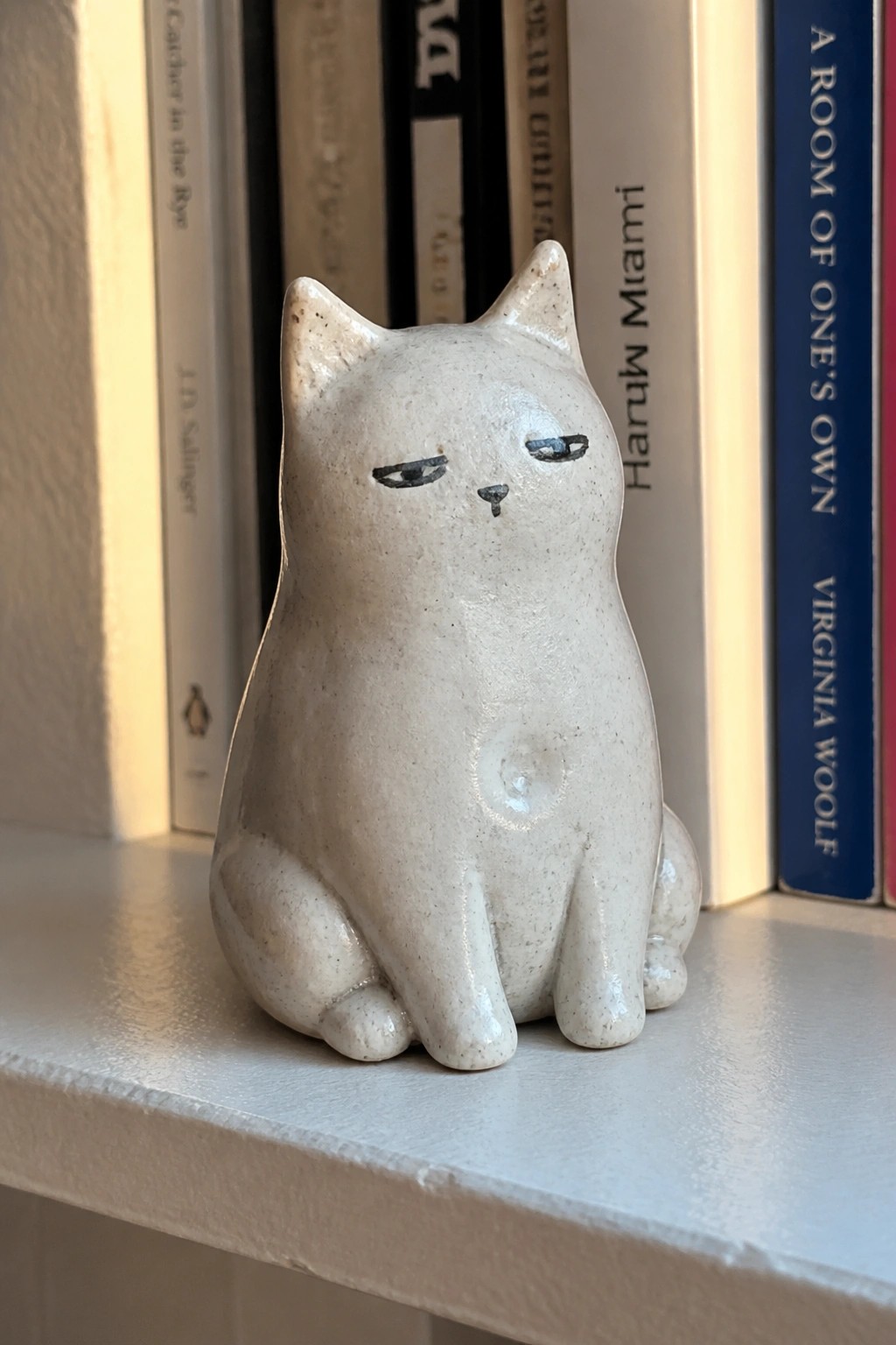 White speckled ceramic cat with squinted eyes on bookshelf with books