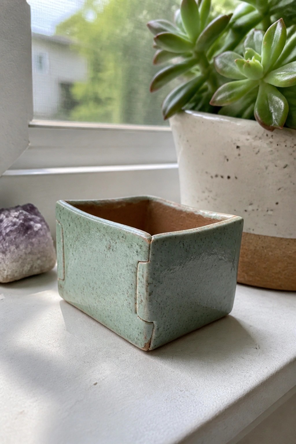 Small green speckled ceramic bowl on white windowsill near amethyst and succulent.