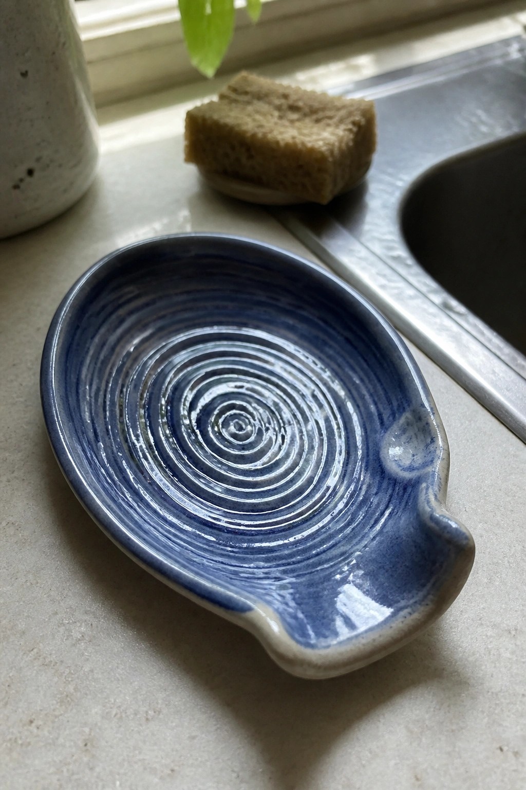 Blue ceramic dish with spiral glaze on countertop beside sink and sponge
