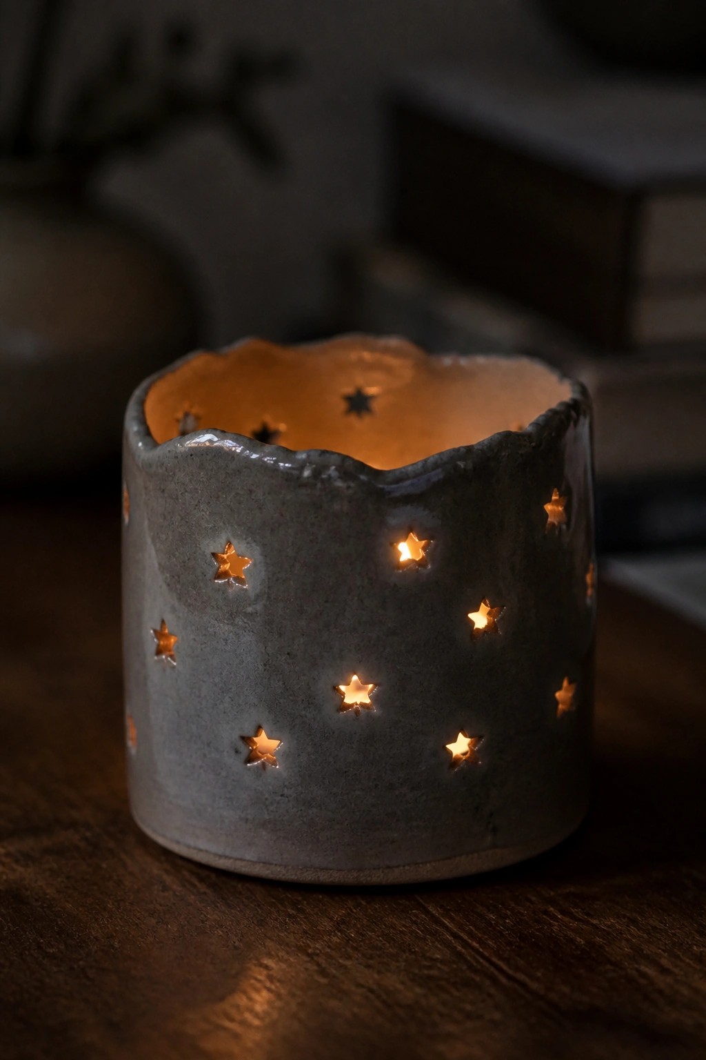 Gray ceramic lantern with glowing star cutouts on dark wooden surface.