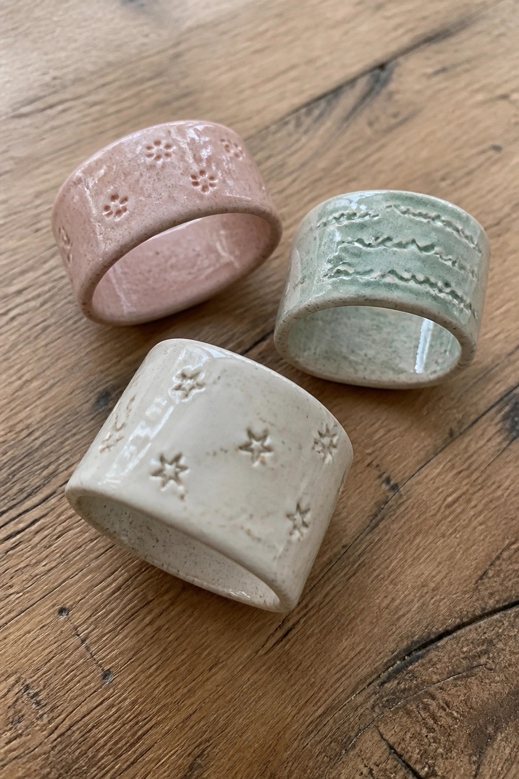 Three ceramic rings in pink, green, and white with embossed flower, wave, and star patterns on wood.