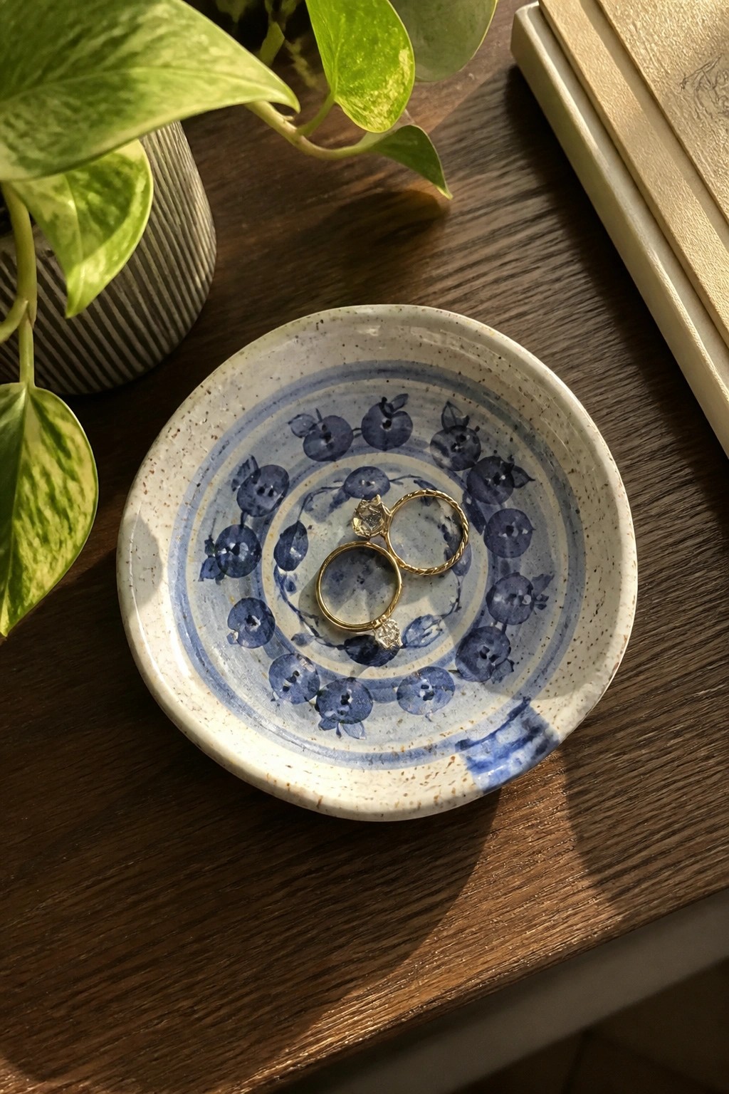 Two gold rings rest in a blue blueberry-patterned ceramic dish on wooden table