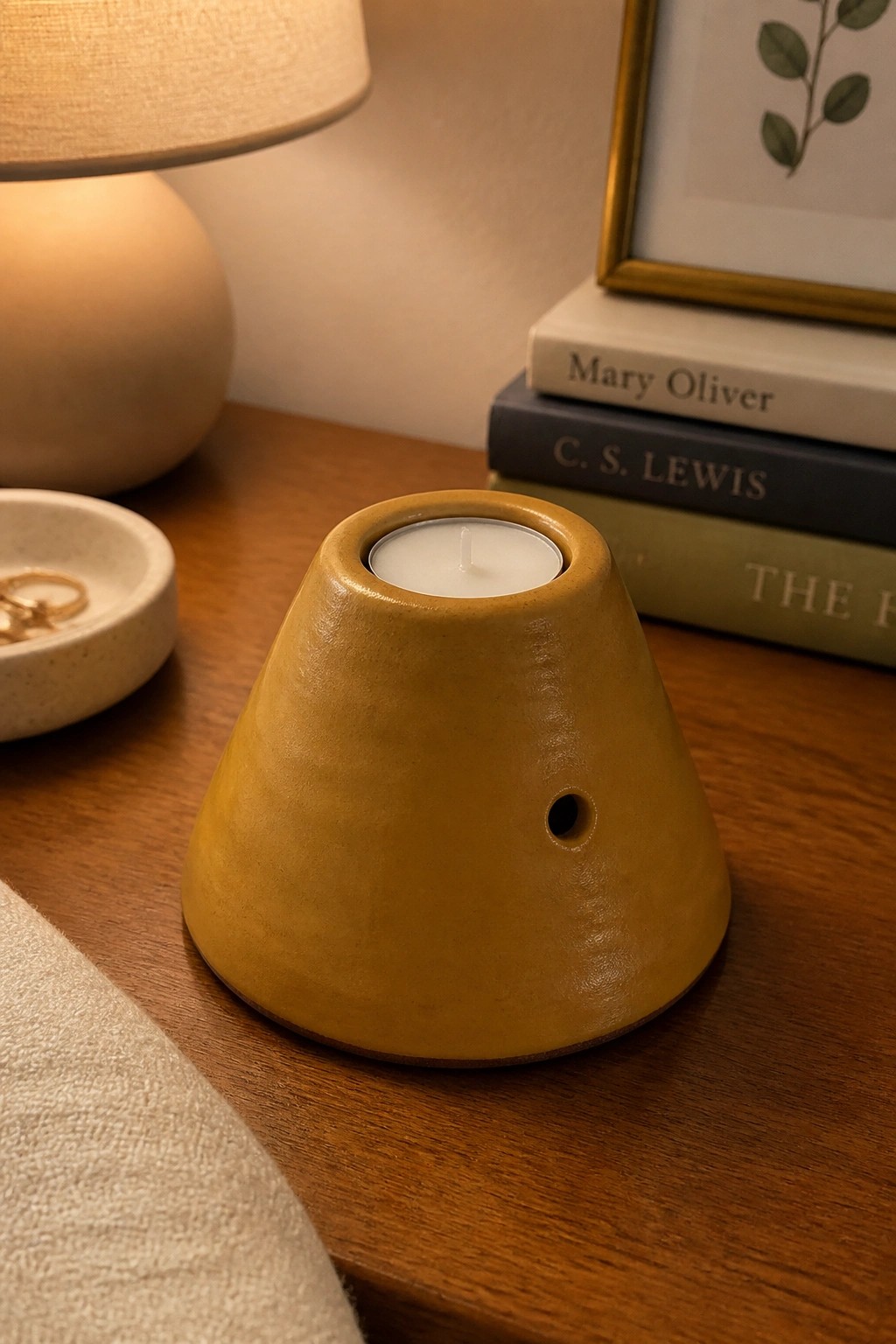 Yellow ceramic tea light holder with lit candle on wooden table near books