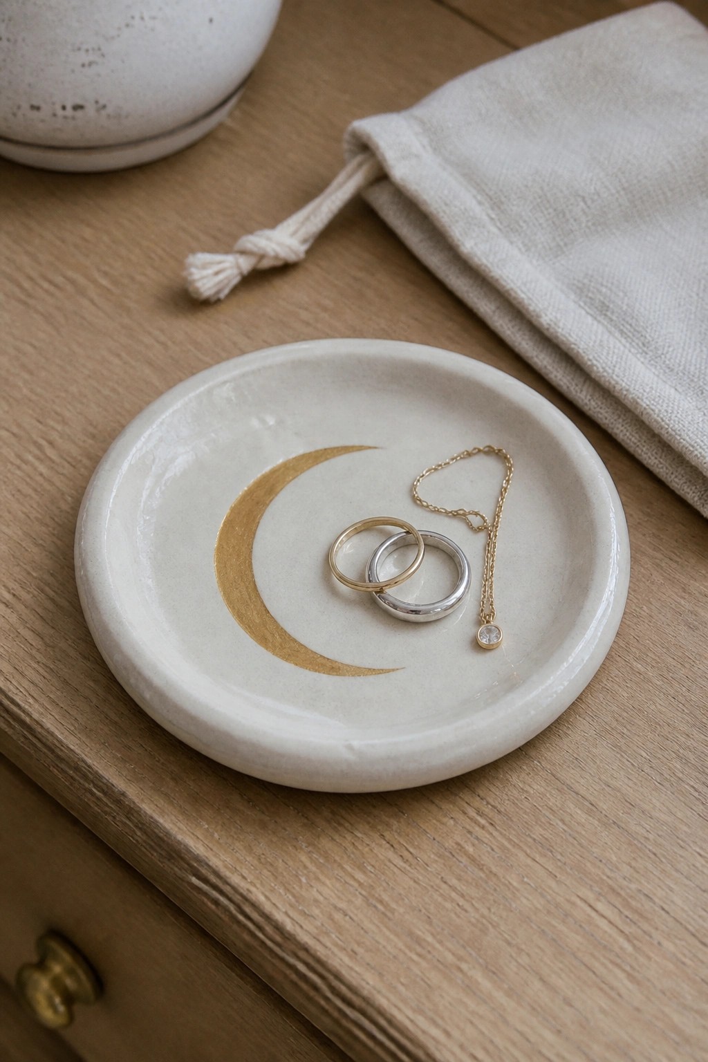 Rings and necklace in white dish with gold crescent moon on wood