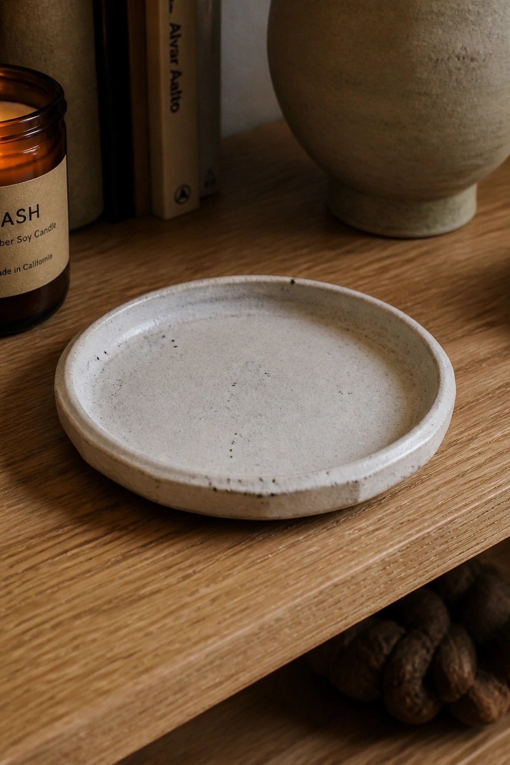 Speckled ceramic plate on wooden shelf near lit candle and books