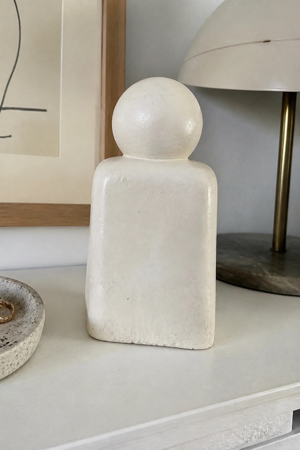 White minimalist sculpture with round head and rectangular body on shelf