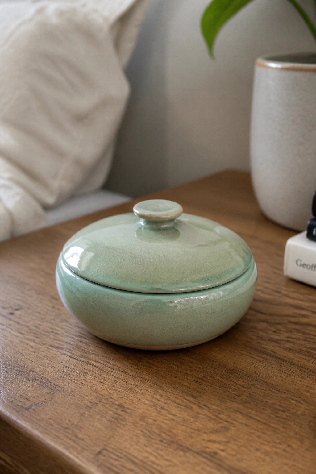 Light green ceramic lidded bowl on wooden table beside white vase