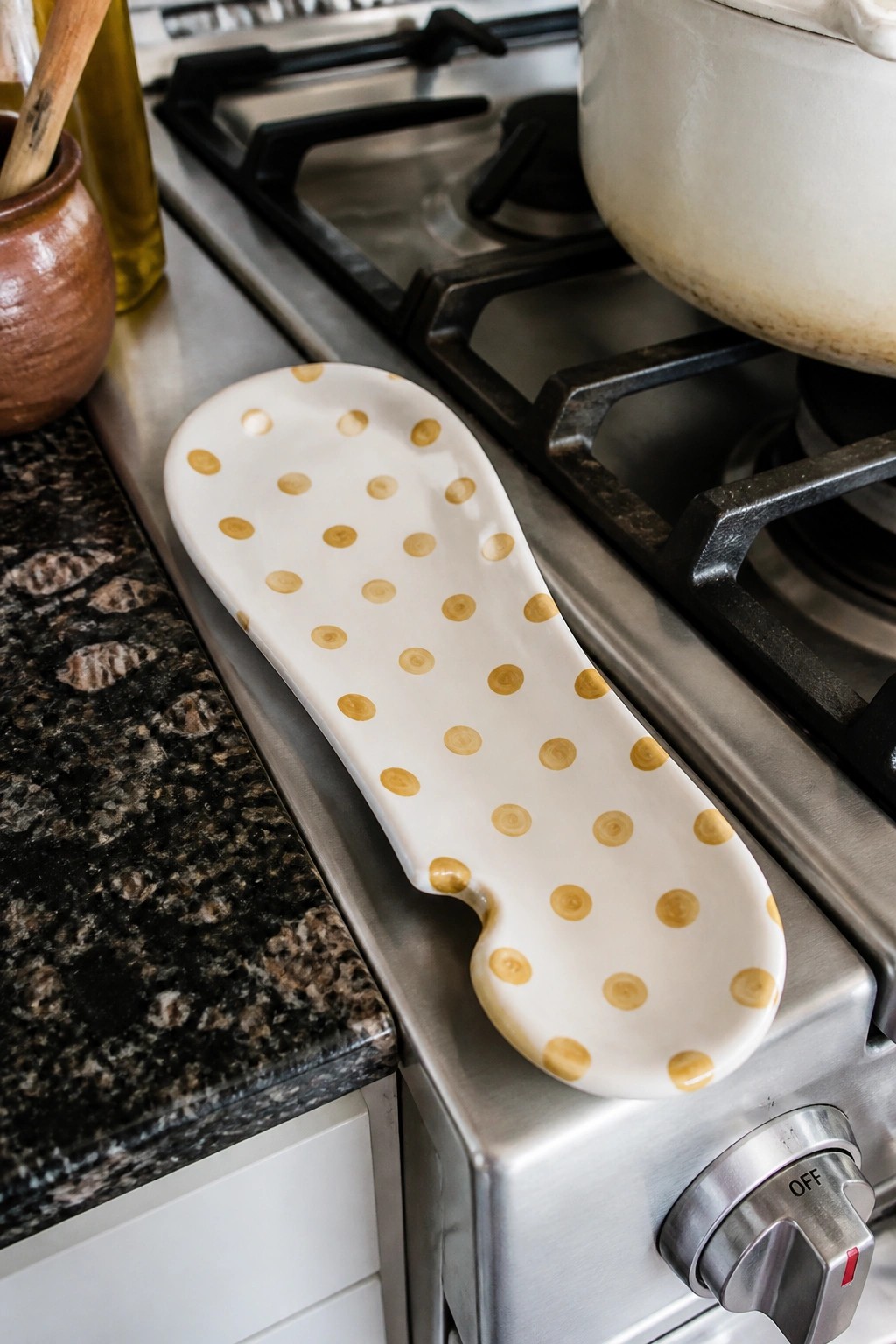 White ceramic spoon rest with gold dots on stainless steel gas stove