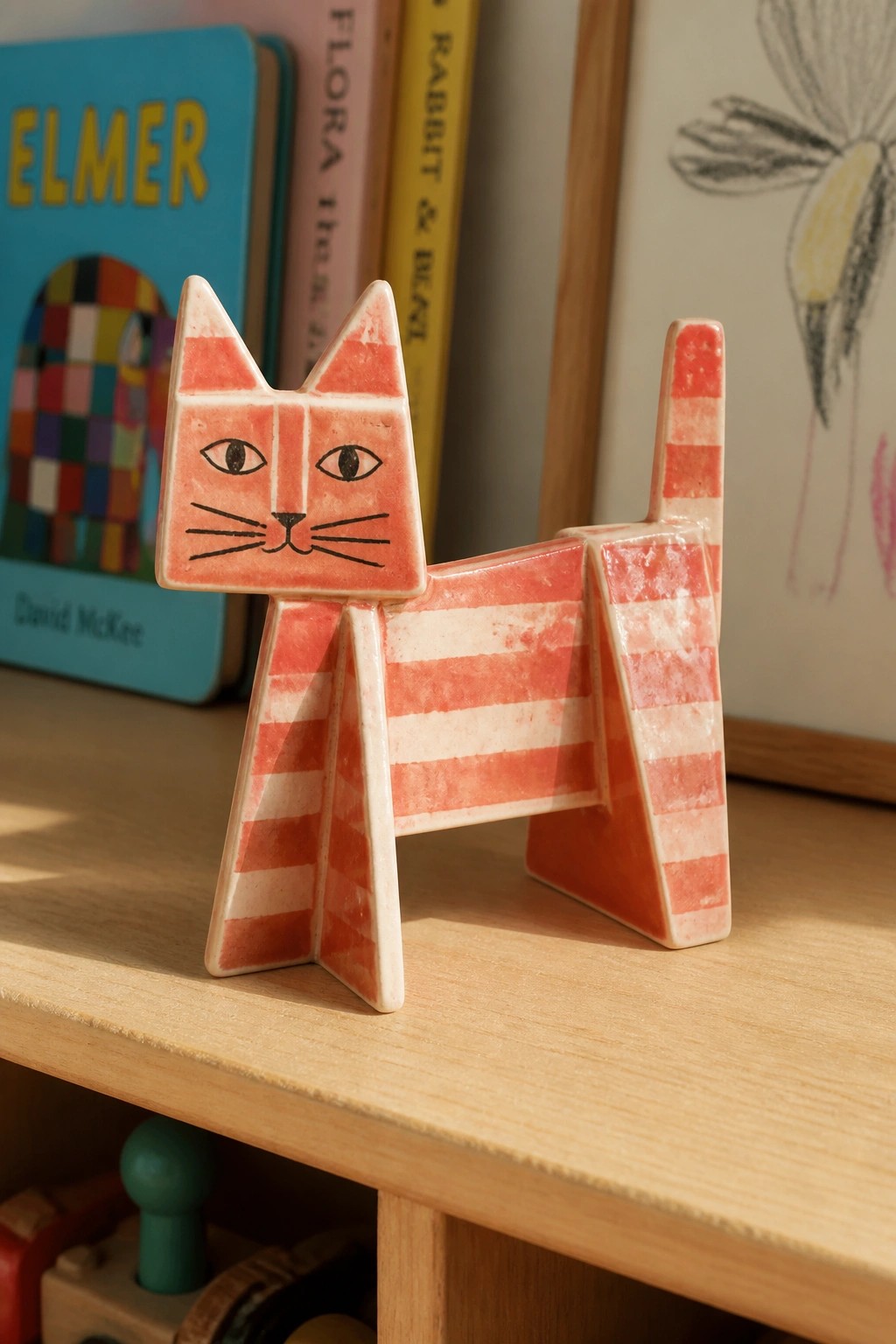Pink and white striped ceramic cat figurine on wooden shelf with books