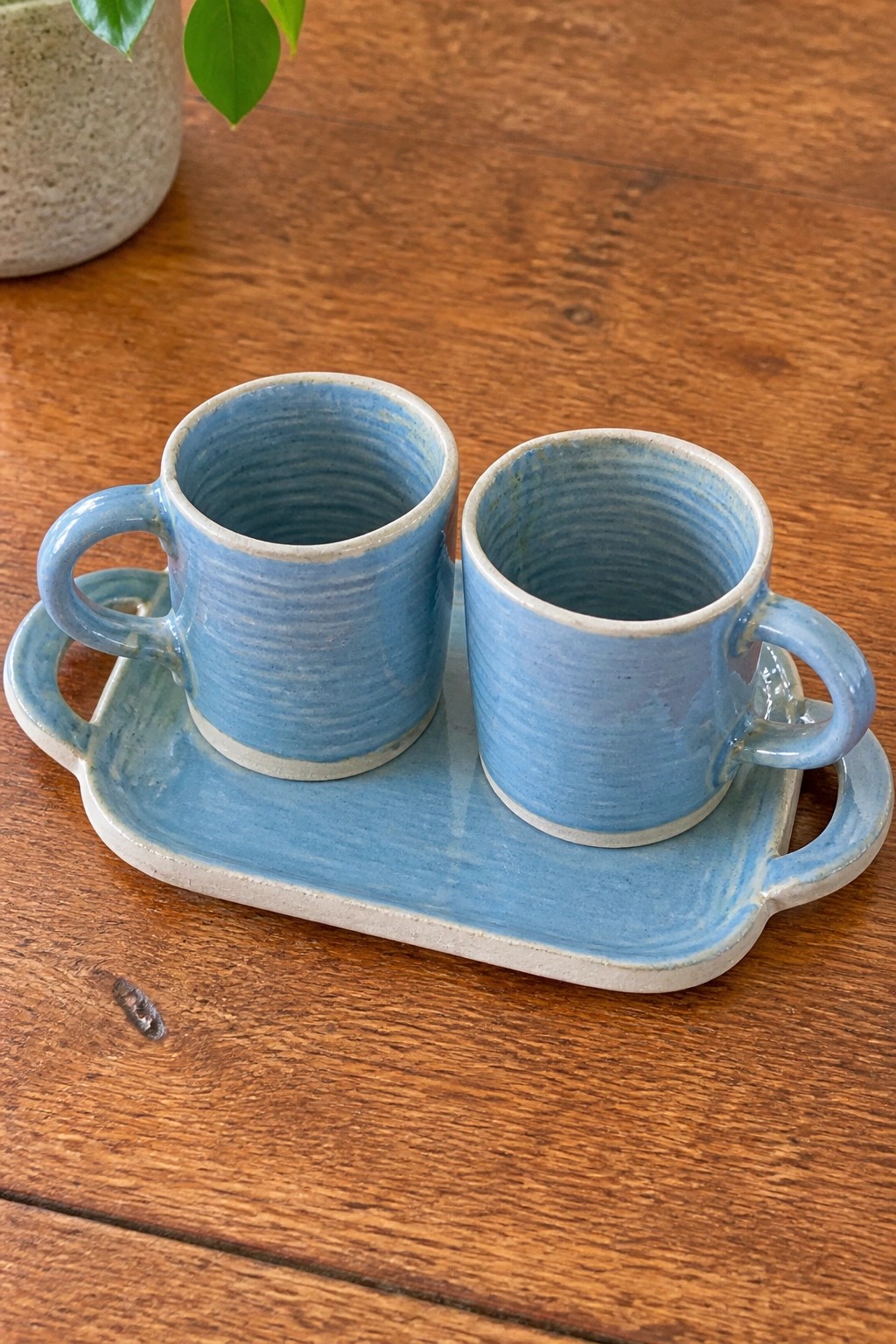 Two blue ceramic mugs on a matching tray atop a wooden table.