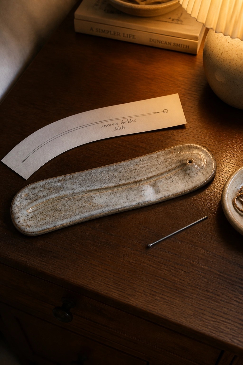Speckled ceramic incense holder on wooden table beside metal pin and paper label