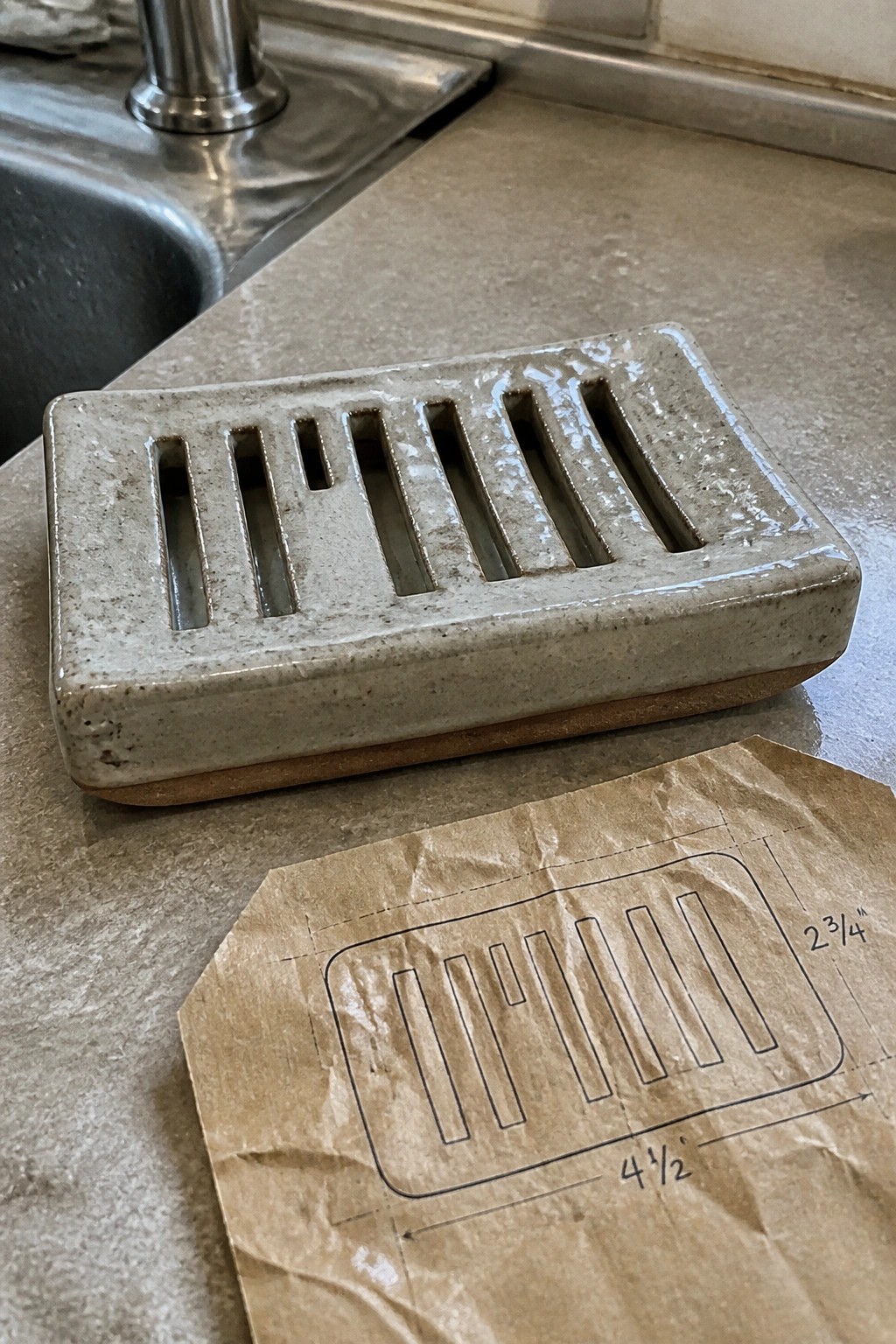 Ceramic soap dish beside paper template with measurements on kitchen countertop