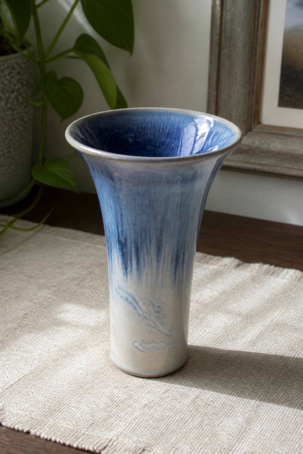 Blue and white ceramic vase with dripping glaze on beige fabric near plant