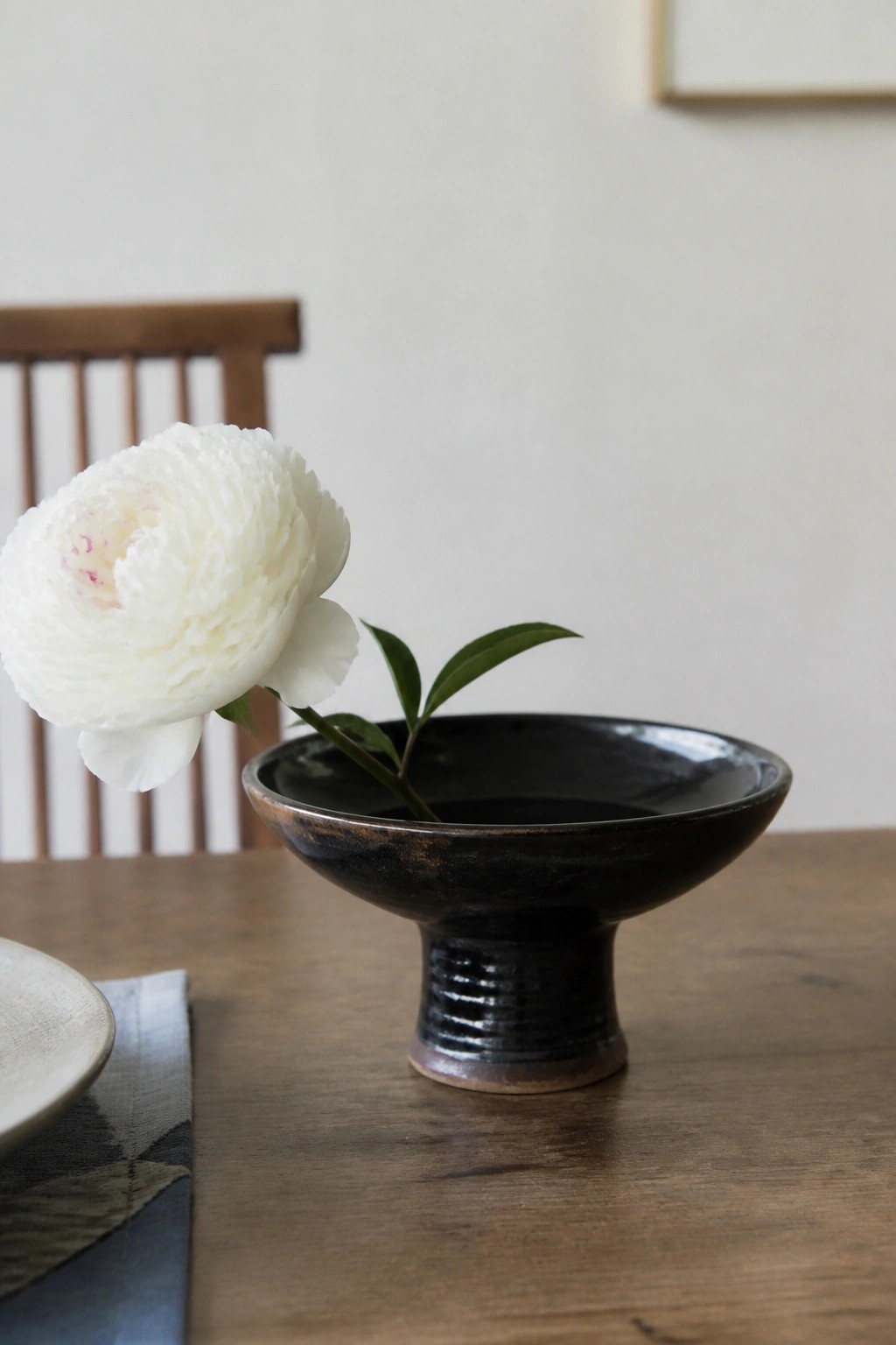 White peony in black ceramic pedestal bowl on wooden table