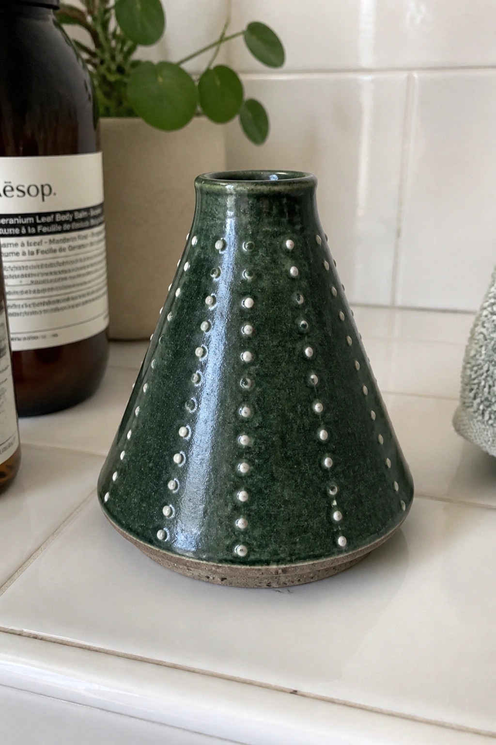 Green ceramic vase with white dots arranged in vertical rows on a white tiled surface.