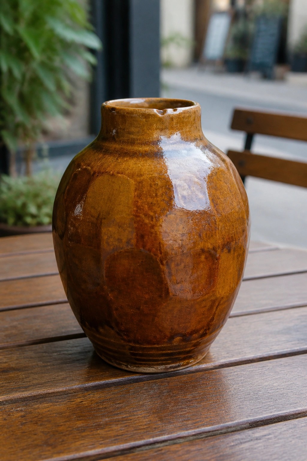 Brown faceted ceramic vase with glossy glaze on wooden outdoor table