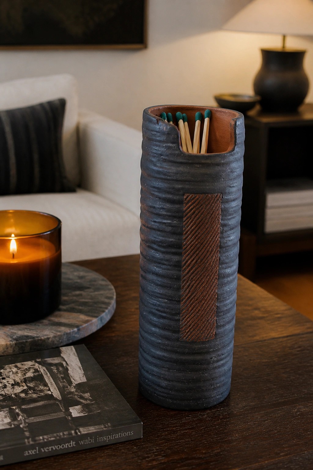 Textured blue ceramic match holder with green-tipped matches on wooden table beside candle