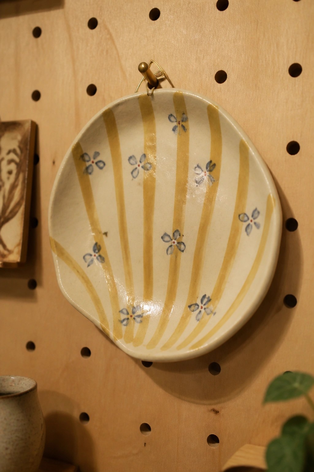 White ceramic bowl with yellow stripes and blue flowers hanging on pegboard.