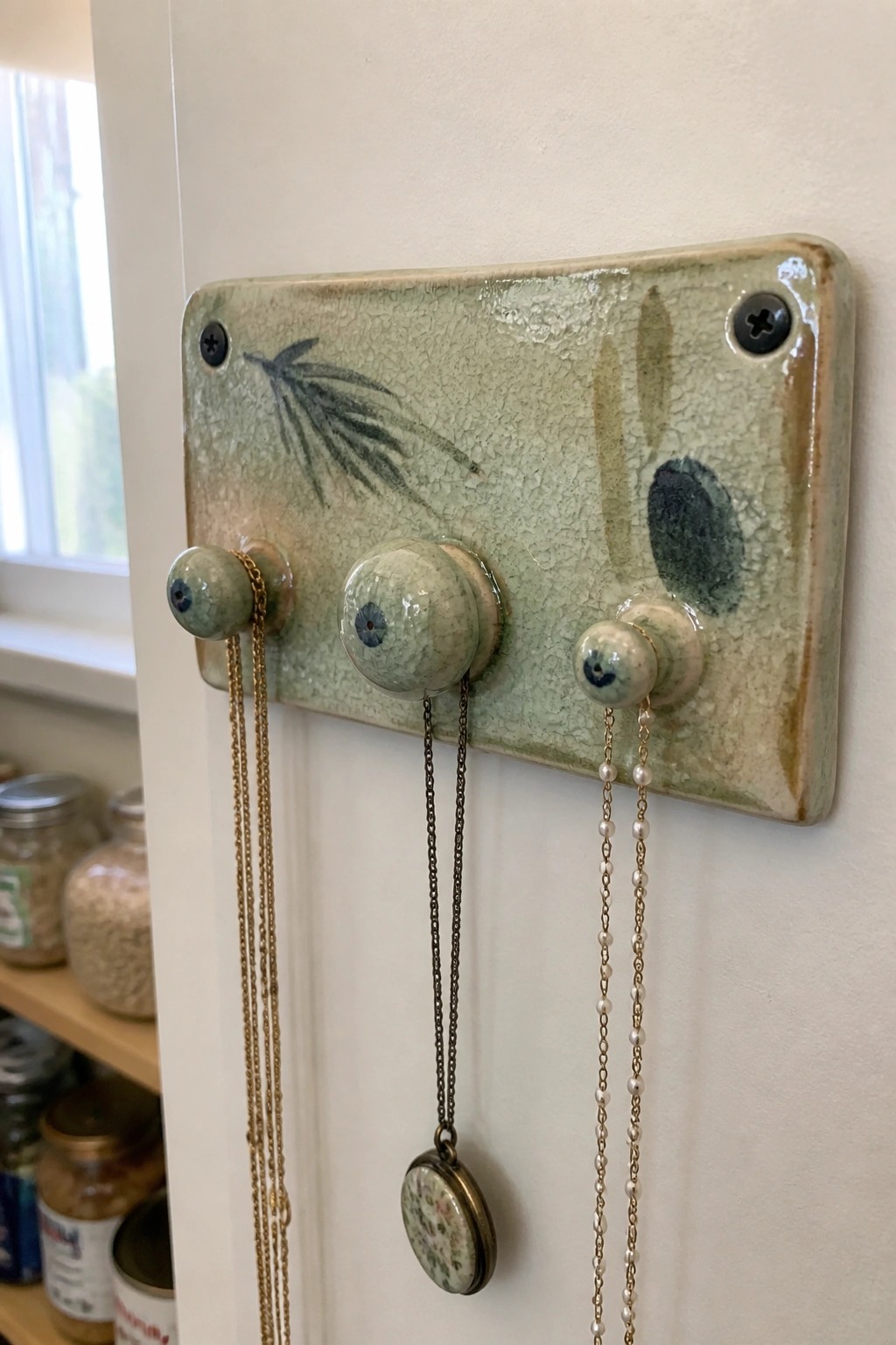 Green crackle-glaze ceramic plaque with three knobs and hanging necklaces on white wall