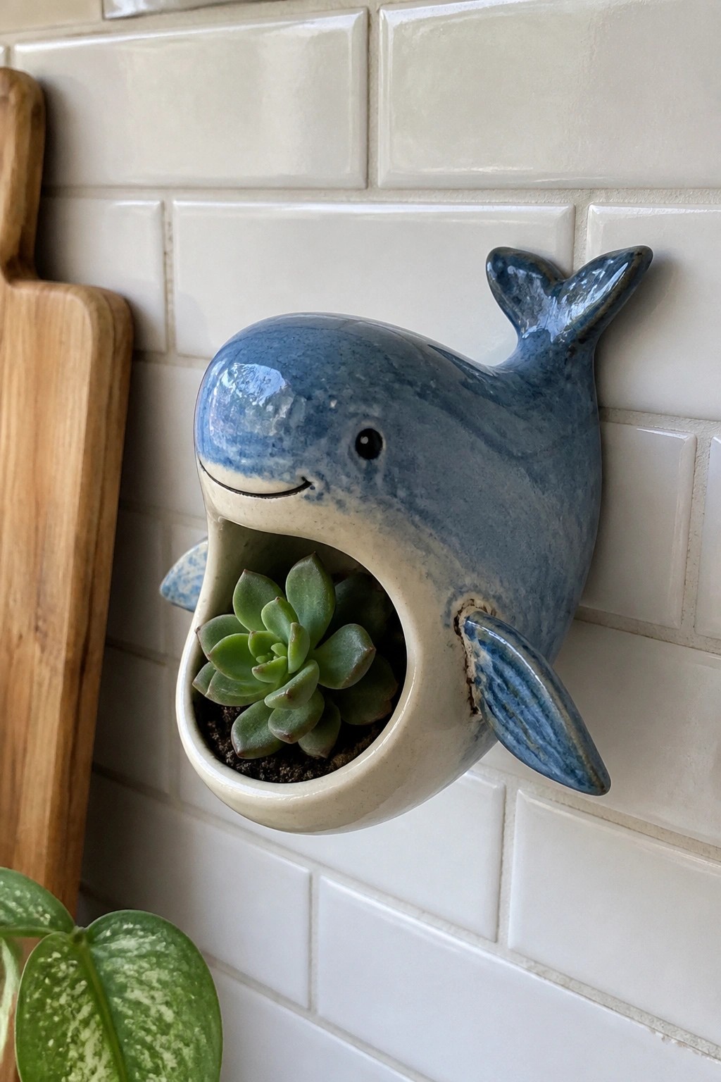 Blue ceramic whale planter holding green succulent on white tiled wall