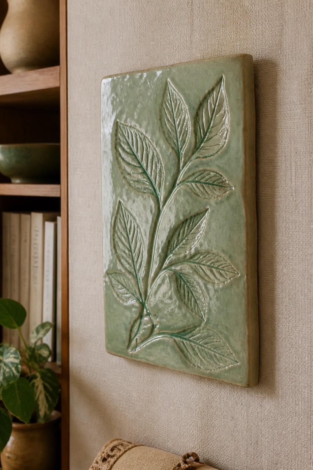 Green glazed ceramic tile with embossed leaves on textured beige wall