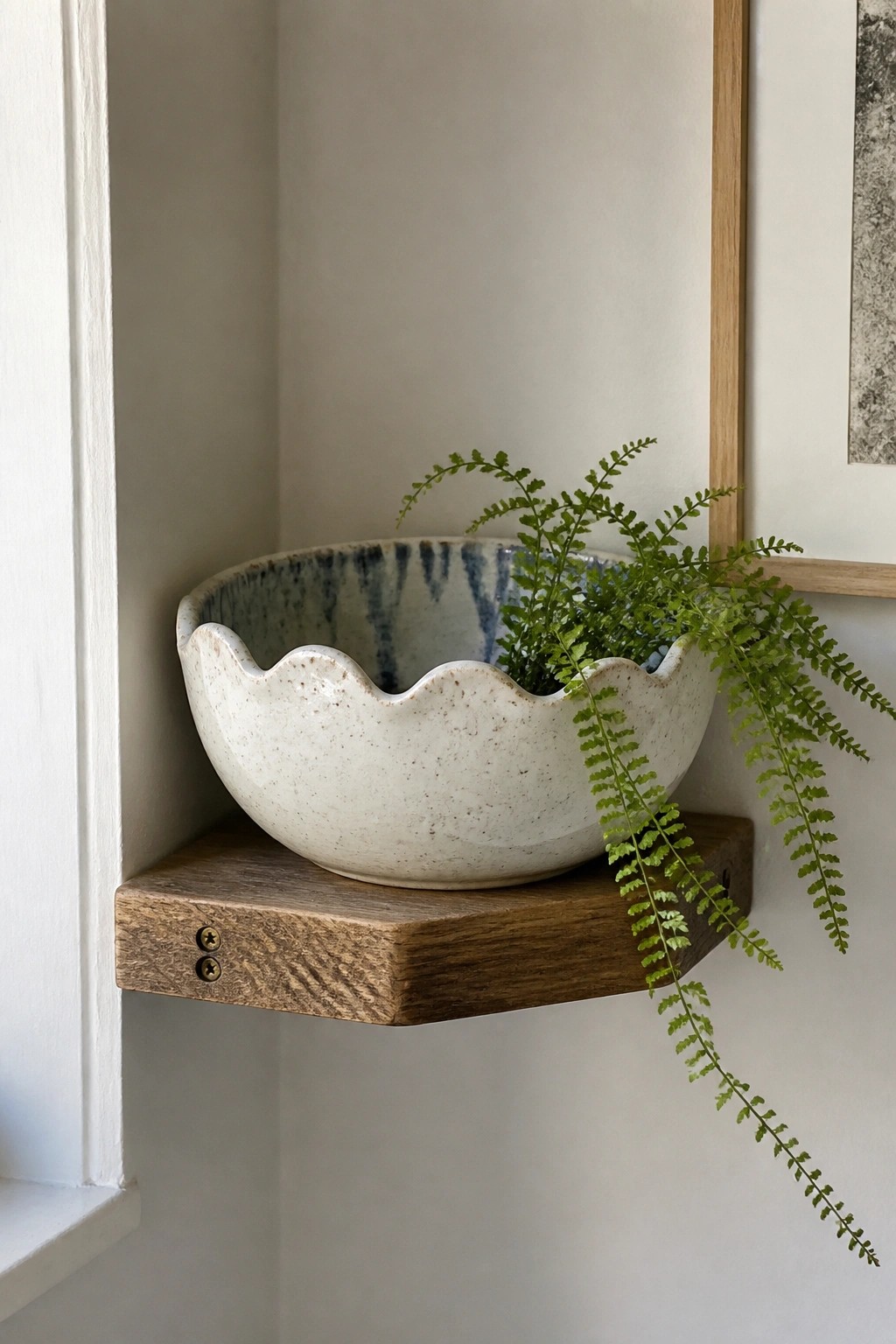 Speckled white ceramic bowl with scalloped rim holding a green fern on wooden shelf
