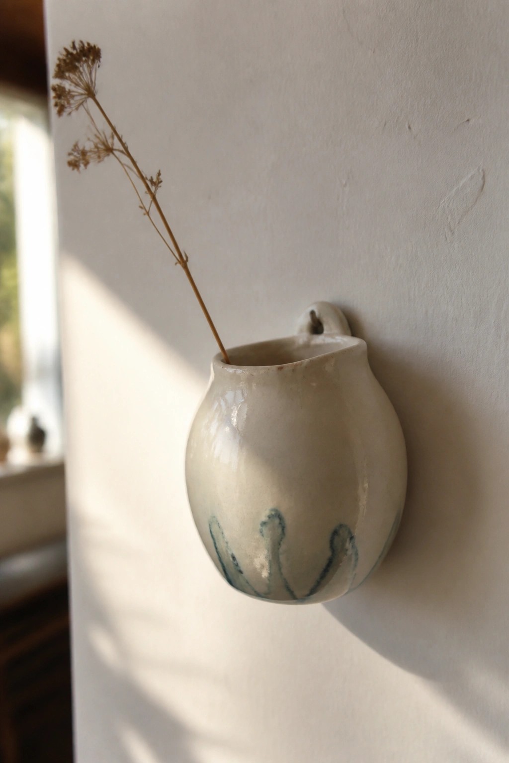Ceramic wall vase with blue patterns holding dried plant stem on white wall