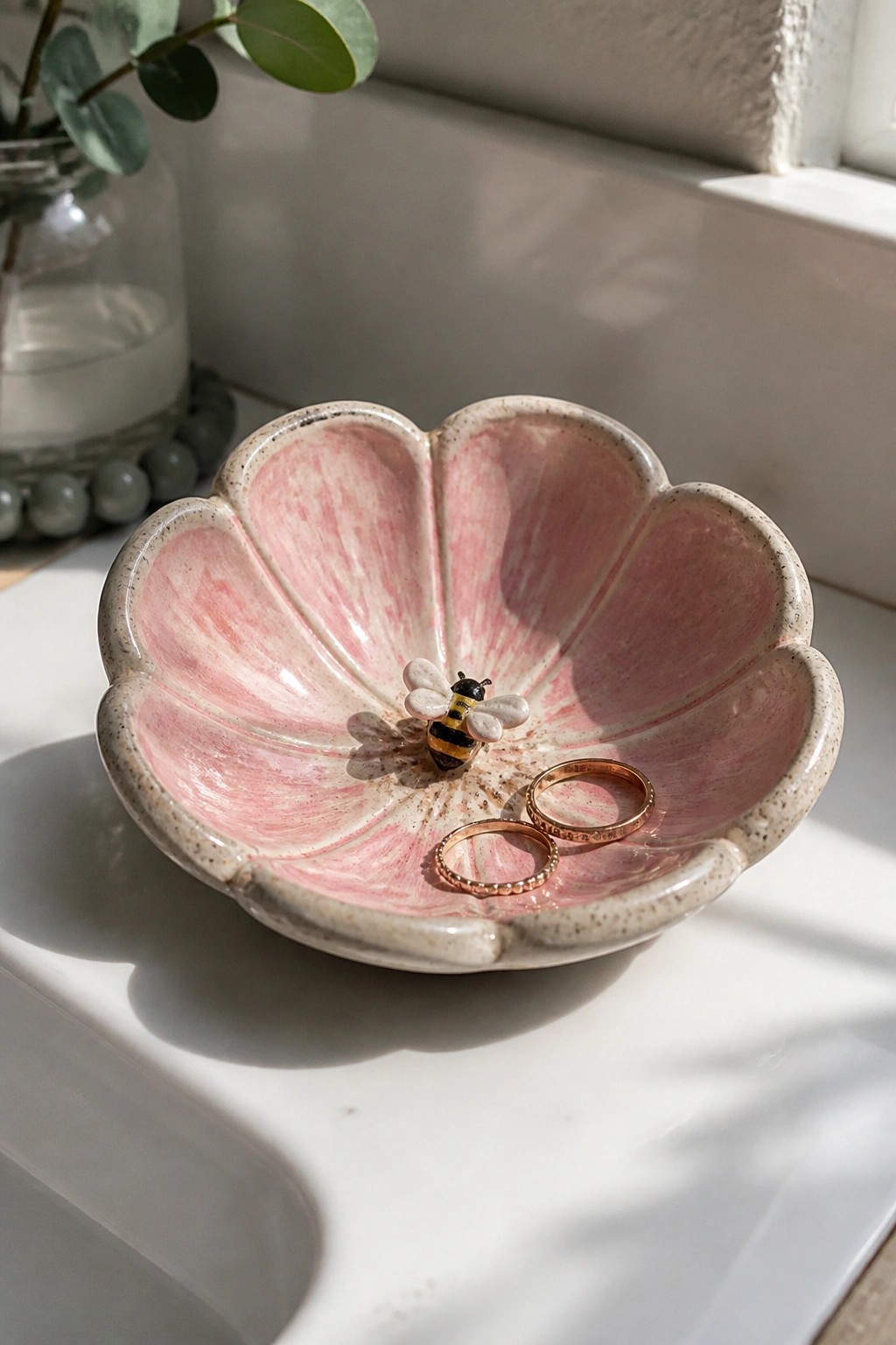 Pink flower-shaped ceramic bowl with bee figurine and two gold rings inside