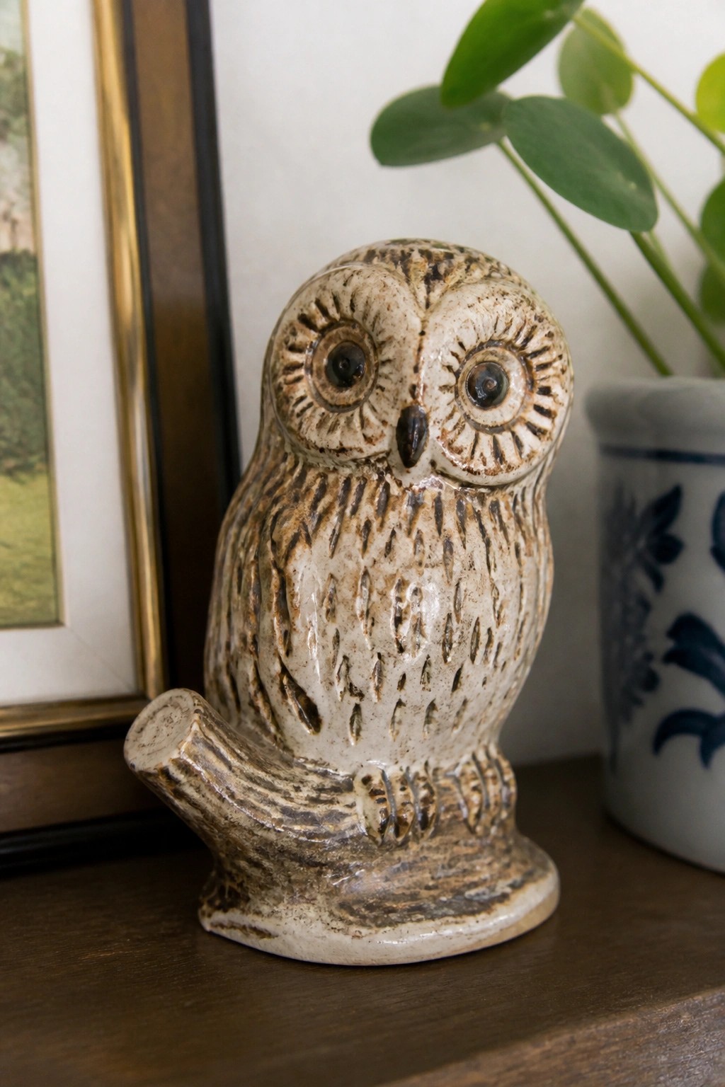 Speckled ceramic owl figurine perched on a branch atop wooden surface
