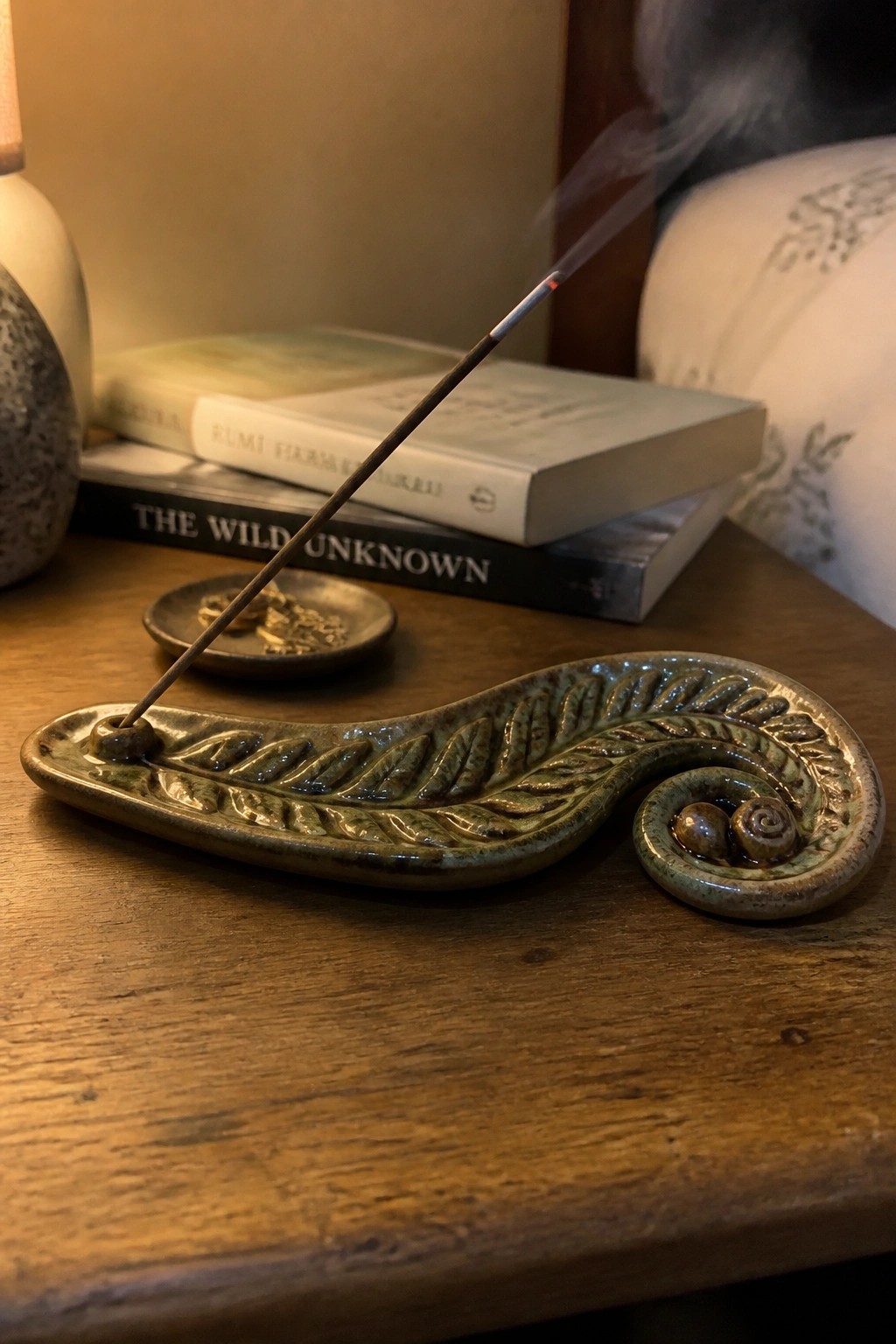 Burning incense in green ceramic leaf holder on wooden table with stacked books