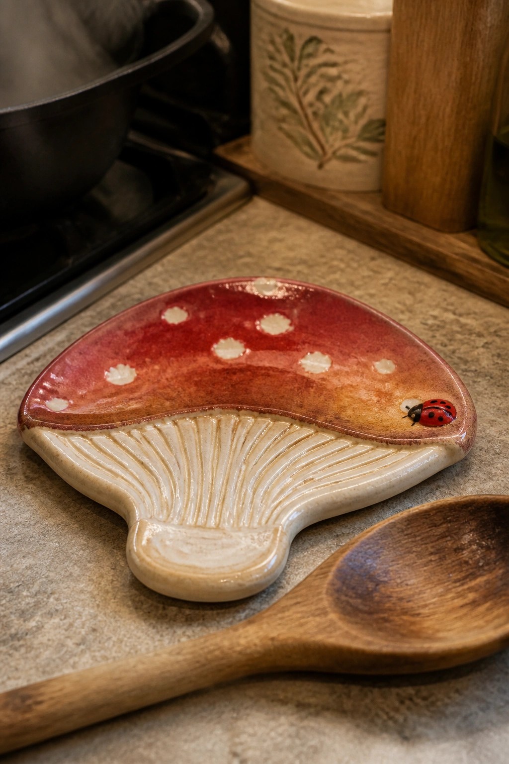 Ceramic mushroom spoon rest with red spotted cap and ladybug beside wooden spoon