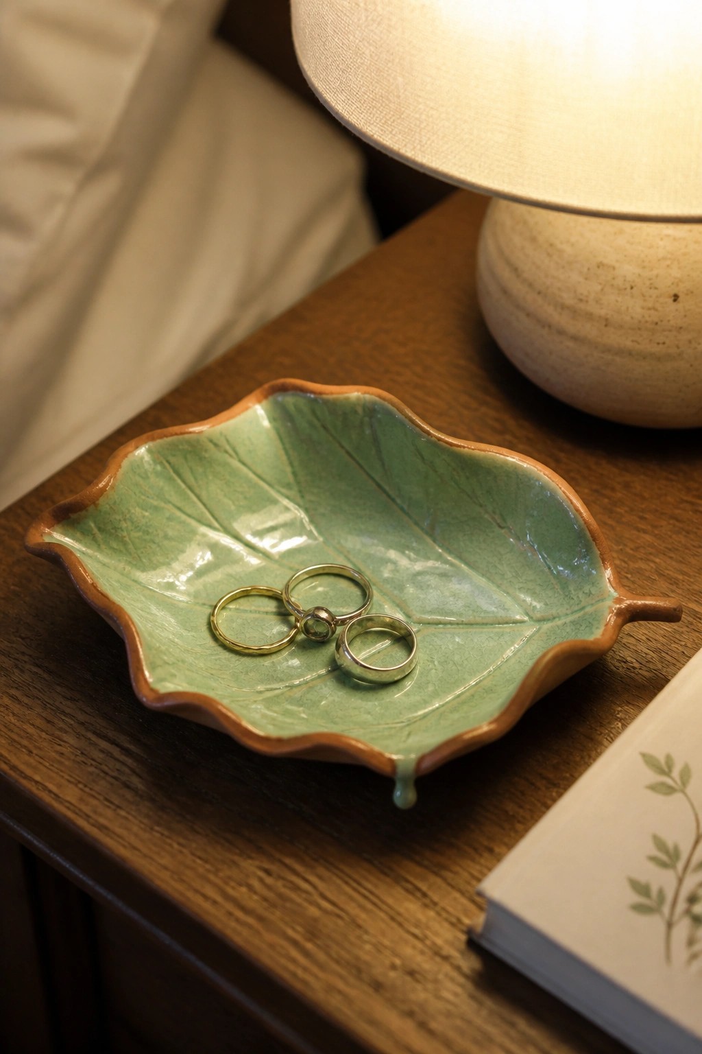 Green leaf-shaped ceramic dish with gold and silver rings on wooden nightstand