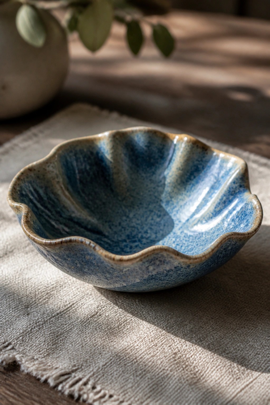Blue ceramic bowl with scalloped rim on textured linen cloth in sunlight.