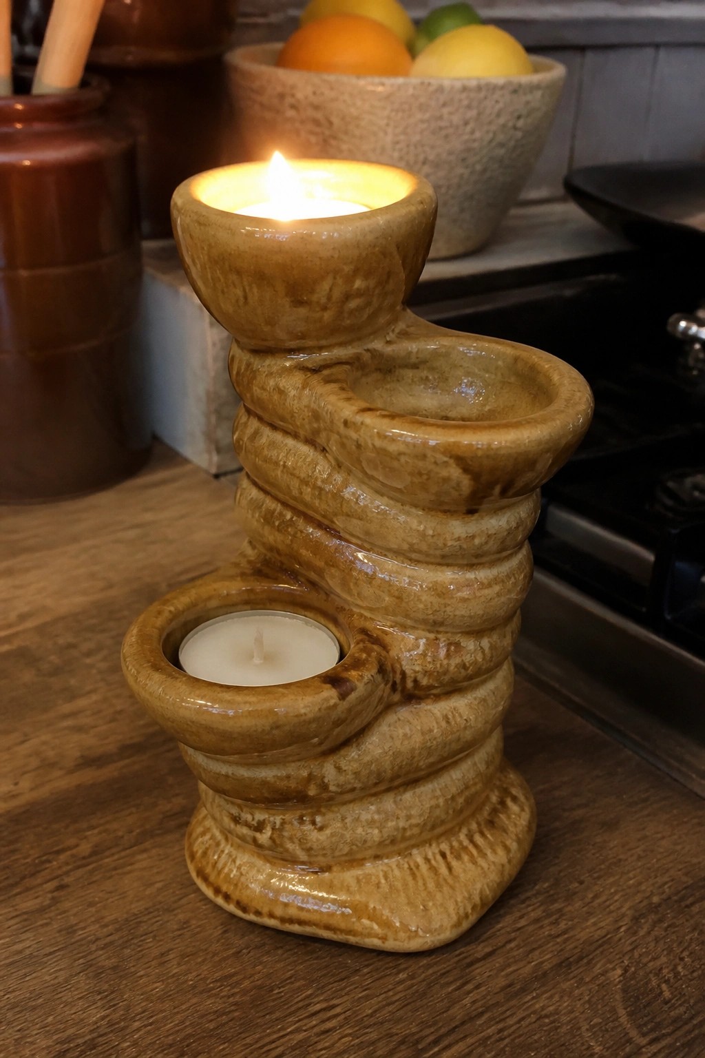 Brown ceramic twisted candle holder with two lit candles on wooden counter.